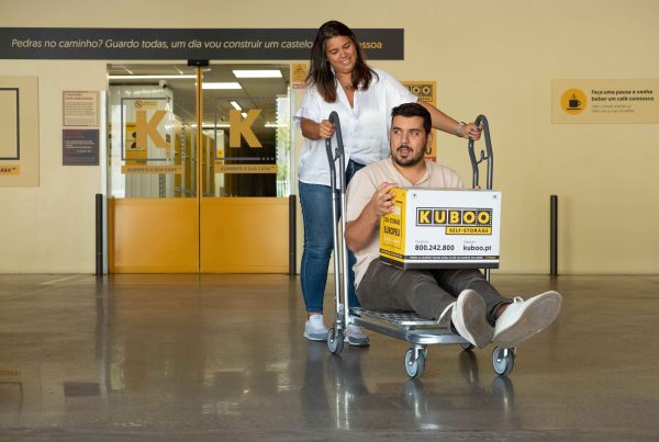 woman pushes man seated on a dolly with a kuboo box on his lap