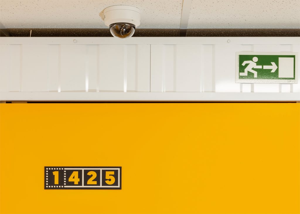 a surveillance camera in front of a kuboo unit with an exit signage next to it