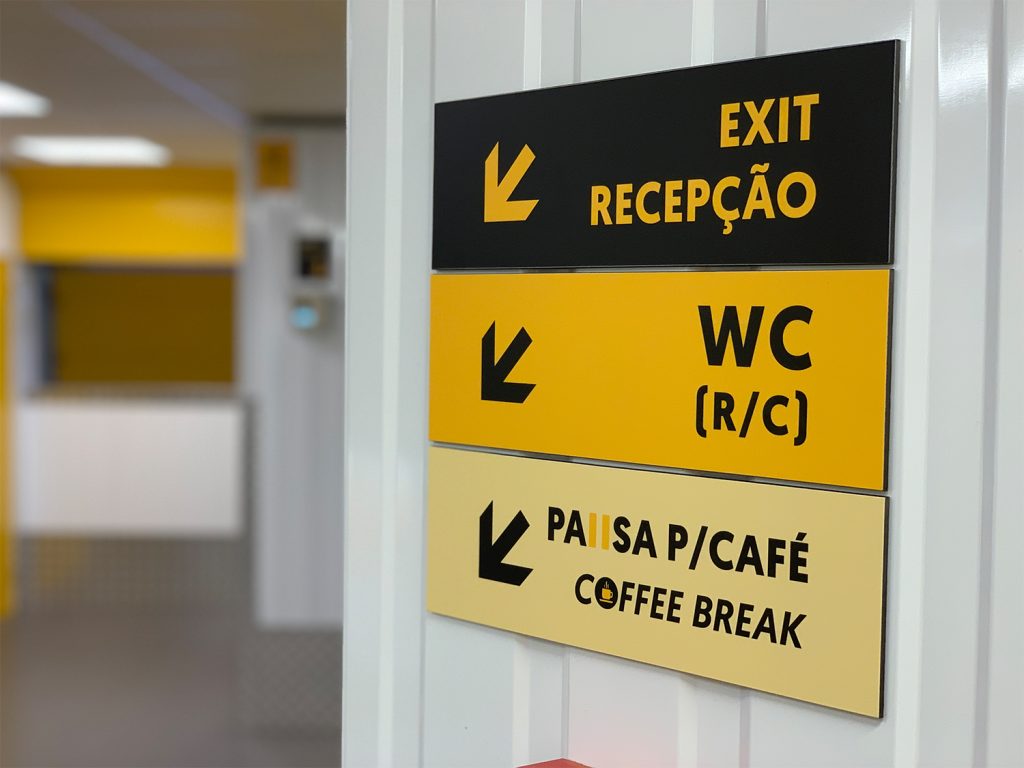 sinalética para a receção, wc e pausa para café num corredor do armazém de carnaxide